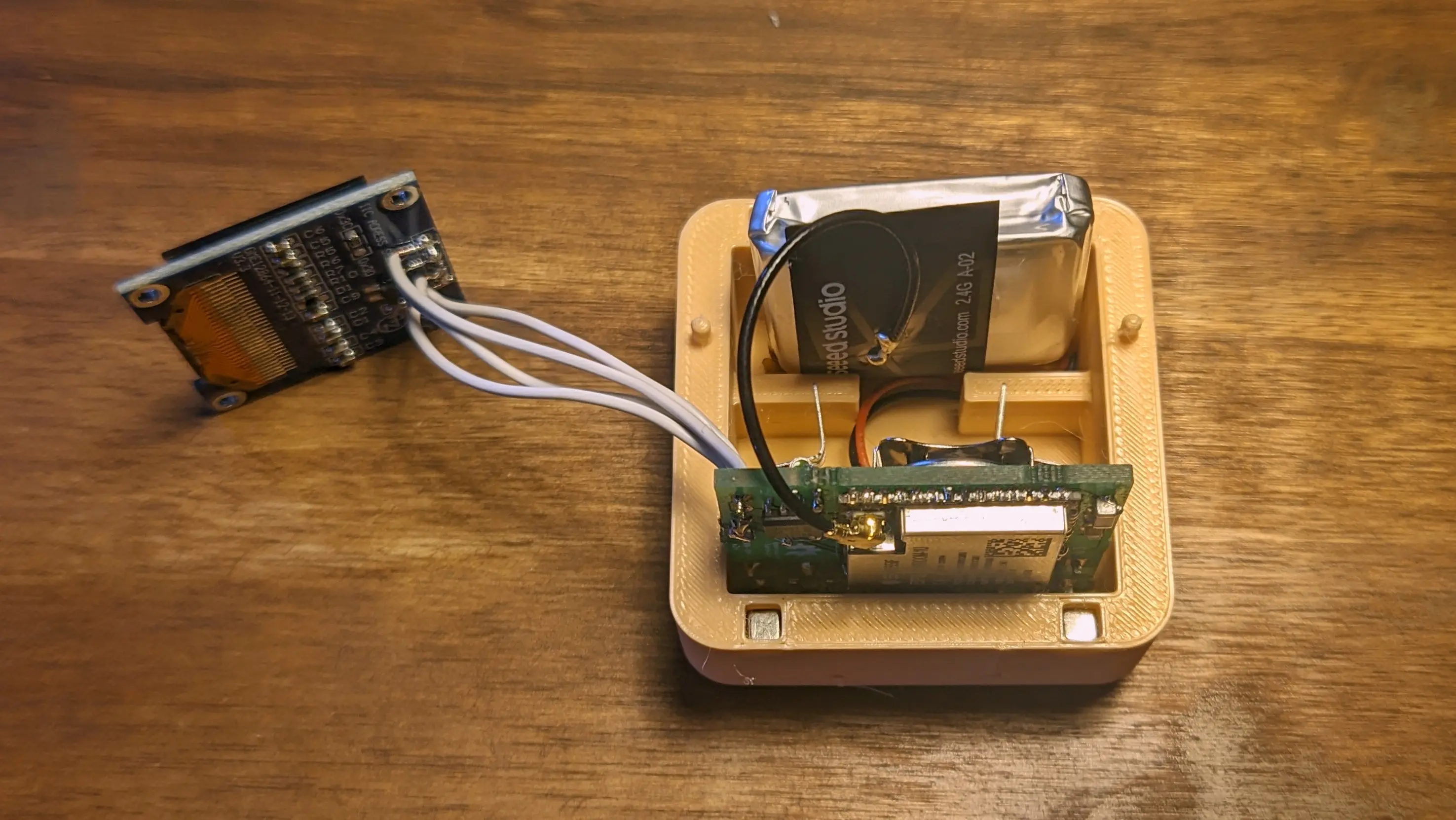 Top down view of the back of the Precious Block case. The PCB has been slotted into the bottom of it and the battery glued into the top section. The antenna is running from the ESP to right below the battery. The display is placed next to the case on the desk, connected to the PCB with four cables